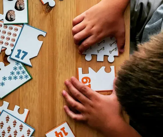 Niño encajando por sí mismo las piezas de un puzle de números sobre una mesa de madera